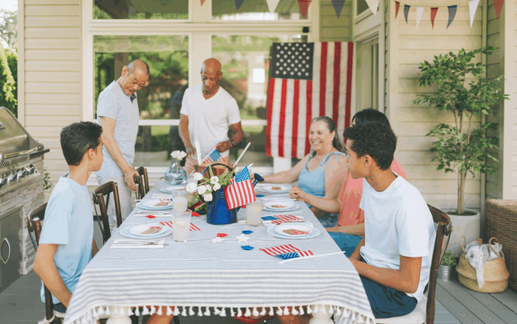 Famílias reunidas ao ar livre comemorando o 4 de julho com churrasco, bandeiras dos EUA e clima festivo típico do Dia da Independência americano.