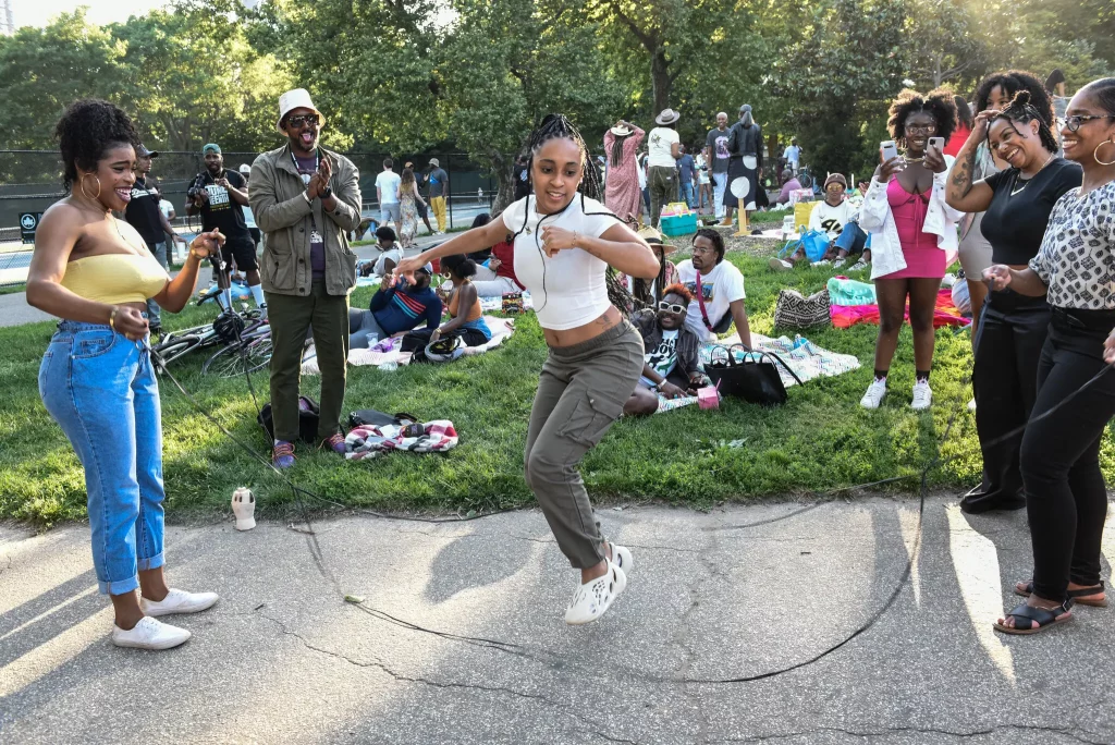 Crianças e adultos participam de brincadeira de double dutch durante comemoração do feriado Juneteenth no Fort Greene Park, Brooklyn, em 2022 — celebração cultural afro-americana nos EUA.