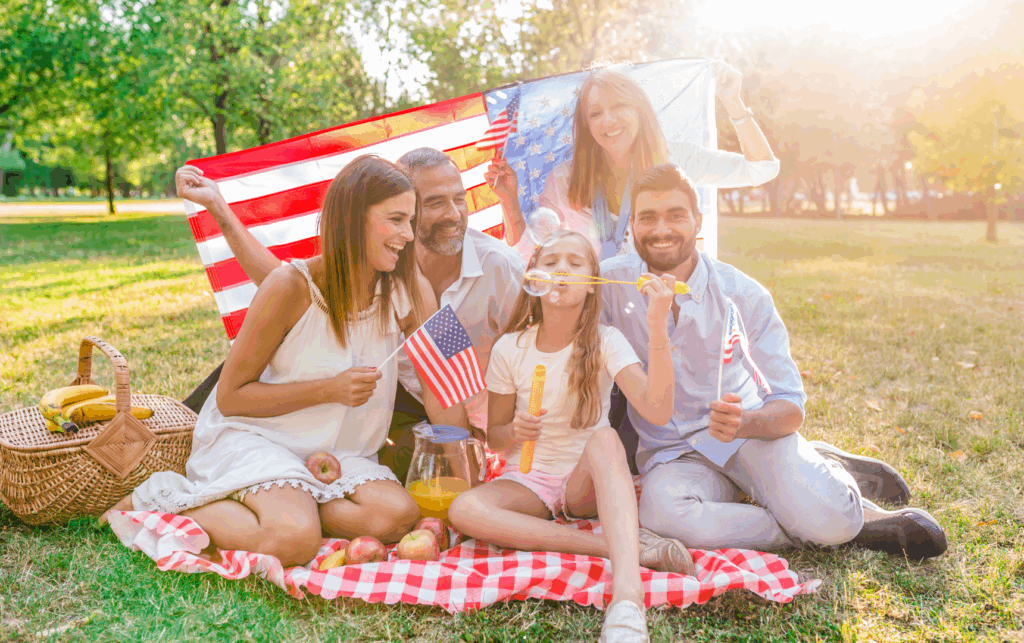 Família americana sorridente comemorando o 4 de julho ao ar livre, com clima de união, bandeiras dos EUA e celebração típica do Dia da Independência.