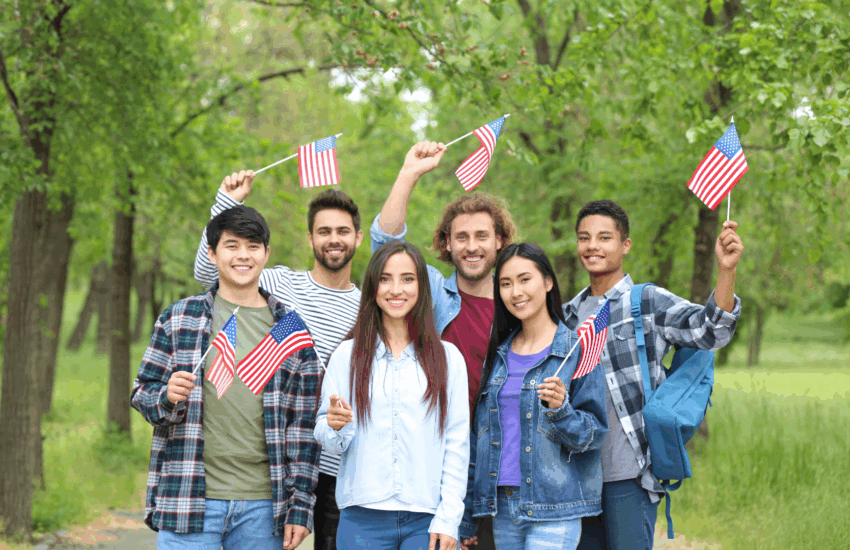 Morar-Eua-SG-Global-Group-Estudar-nos-EUA-como-escolher-universidade-e-requisitos Grupo de estudantes internacionais felizes segurando livros e a bandeira dos Estados Unidos, simbolizando o sonho de estudar nos EUA e a busca por educação de qualidade.